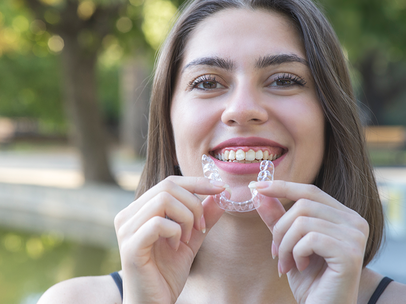Dental services- Invisalign, image of a young woman holding her Invisalign while smiling