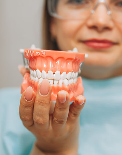 Dentures, image of a Woman holding a tooth sample or denture at the dentist.