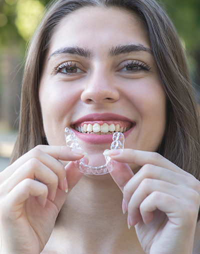 Invisalign, image of a young woman holding her Invisalign while smiling