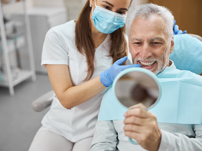 dental services, Dental Implants, image of a bearded older man smiling at the dentist after getting his dental implants