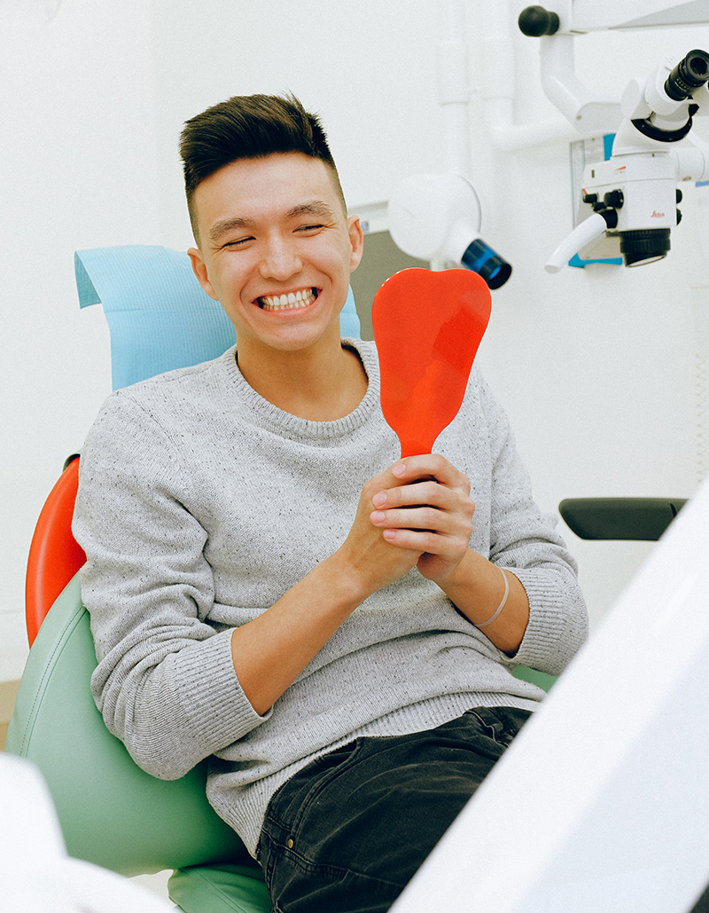 Welcome to Oasis Dental Arts, Proudly providing dental services in the Scripps Ranch and Mira Mesa Areas, image of a young man smiling with a mirror.